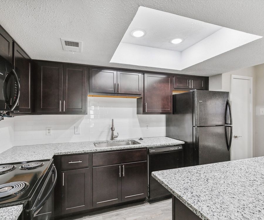 Crossings on Marsh modern kitchen features dark cabinets, granite countertops, black appliances, and a stunning skylight.