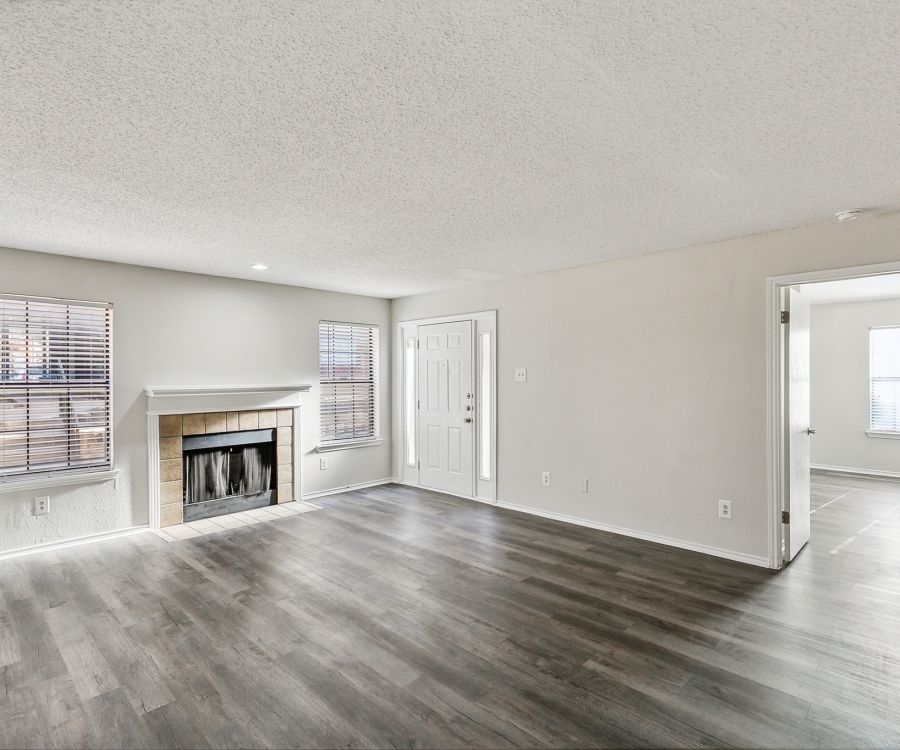 The spacious living room at Crossings on Marsh apartments features a cozy fireplace, large windows, and sleek gray wood flooring, seamlessly leading to an adjacent room.