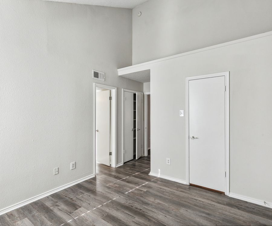 The empty room in Crossings on Marsh apartments features gray walls, a wooden floor, two white doors, and a high ceiling.